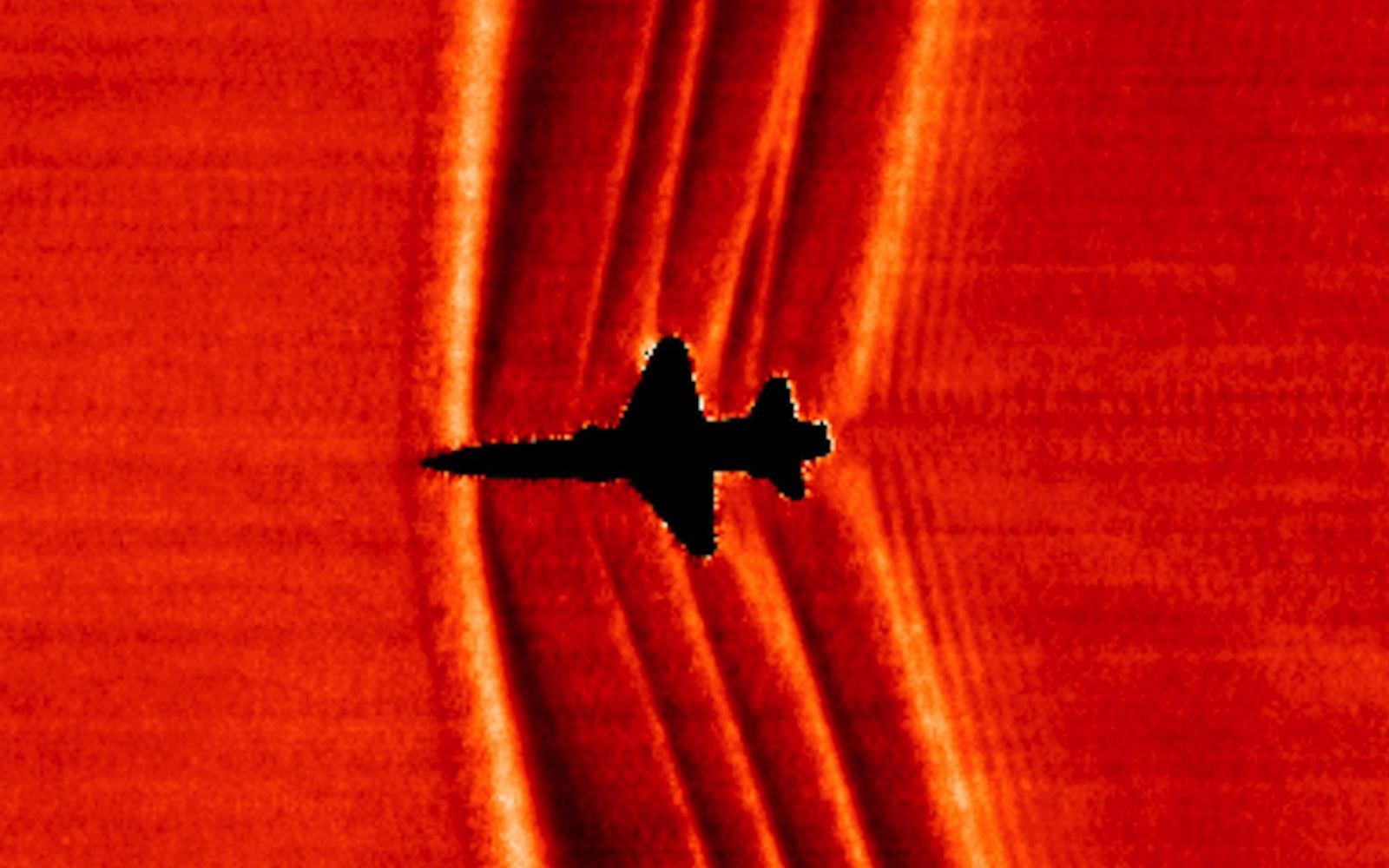 NASA background-oriented schlieren photograph of a T-38C in supersonic flight, silhouetted against the sun, with its shock system visible as bright and dark bands